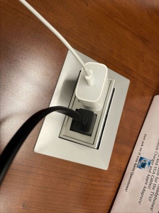 A white electrical outlet with a black cord plugged into it Description automatically generated